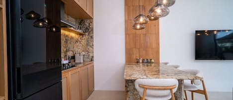 Uma cozinha moderna com geladeira preta, armários de madeira, ilha de granito e luminárias pendentes.
