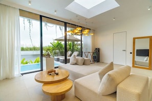 Ein modernes Wohnzimmer mit einer Couch, einem runden Holztisch und einem großen Fenster mit Blick auf Grünflächen und einen Pool.