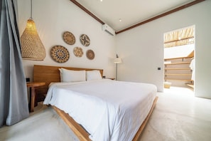 A bedroom with a large bed, a wooden headboard, a hanging light fixture, and decorative plates on the wall. - Tropical 2BR in Serene Ubud w Pool & Huge Garden (Ubud)