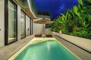 A swimming pool with two lounge chairs and an umbrella, surrounded by lush greenery. - Designer 2BR in Ungasan w Pool & Beach Access (Badung Regency)
