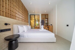 Une chambre d’hôtel moderne avec un grand lit, une tête de lit en bois, une petite table ronde et une armoire.
