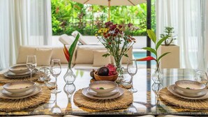 Uma mesa de jantar posta com pratos, tigelas e copos, rodeada de cadeiras, com vista para o verde lá fora.
