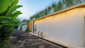 Um caminho leva a um edifício com telhado plano, um vaso com plantas e uma parede com iluminação embutida.