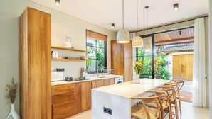 A modern kitchen with wooden cabinetry, a central island, and bar stools. - Designer 2BR Villa in Serene Ubud w Pool & Garden (Gianyar Regency)