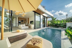 Ein modernes Haus mit Swimmingpool, Sitzgelegenheiten im Freien und einem großen Sonnenschirm.