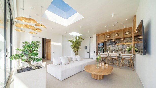 Un espacio moderno para vivir con un sofá blanco, una mesa de centro redonda de madera y una zona de comedor con sillas.