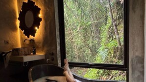 A bathtub with a person sitting inside, a candle, and a bottle on a side table. - Jungle Villa, Brand New, Unique Art Design, Pool (Gianyar Regency)