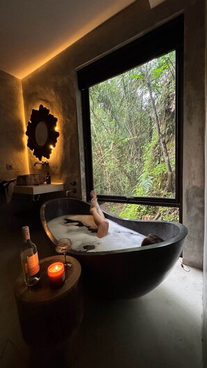 A bathtub with a person sitting inside, a candle, and a bottle on a side table. - Jungle Villa, Brand New, Unique Art Design, Pool (Gianyar Regency)