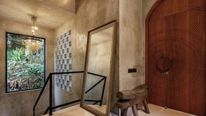 A staircase with a large mirror, a wooden door with a circular pattern, and a window with a view of greenery. - Jungle Villa, Brand New, Unique Art Design, Pool (Gianyar Regency)