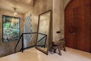 A staircase with a large mirror, a wooden door with a circular pattern, and a window with a view of greenery. - Jungle Villa, Brand New, Unique Art Design, Pool (Gianyar Regency)