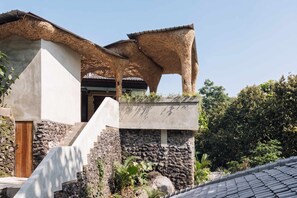 A building with a stone facade, a wooden door, and a thatched roof structure. - Jungle Villa, Brand New, Unique Art Design, Pool (Gianyar Regency)