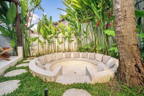 A circular outdoor seating area with a concrete floor and cushioned benches, surrounded by lush greenery and a tree trunk. - Huge Tropical 3BR in Serene Ubud w Pool & Lounge (Ubud)