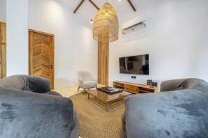 A modern living room with a large TV, two sofas, a coffee table, and a unique hanging light fixture. - Huge Tropical 3BR in Serene Ubud w Pool & Lounge (Ubud)