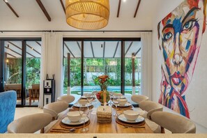 A dining area with a table set for six, large windows, and a painting on the wall. - Huge Tropical 3BR in Serene Ubud w Pool & Lounge (Ubud)