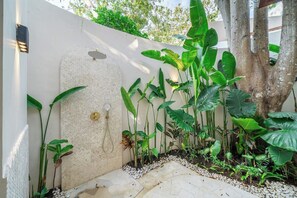 Ein Gartenbereich mit weißer Mauer, einem Baum und verschiedenen Pflanzen.