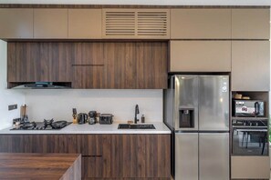 A modern kitchen with wooden cabinets, stainless steel appliances, and a built-in oven. - Chic 4BR Villa w/ Private Massage Room & Huge Pool (Badung Regency)