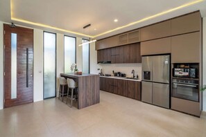 A modern kitchen with a central island, stainless steel appliances, and a minimalist design. - Chic 4BR Villa w/ Private Massage Room & Huge Pool (Badung Regency)