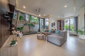 Ein geräumiges Wohnzimmer mit einem Ecksofa, einem Couchtisch und einem großen Fenster mit Blick auf Grünflächen.