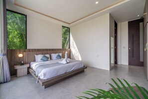 Ein modernes Schlafzimmer mit einem großen Bett, Nachttischen und Blick auf Grün hinter den Fenstern.