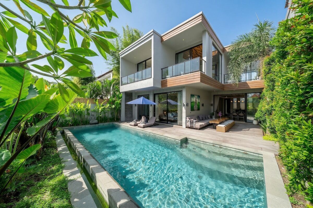 Una moderna casa a due piani con piscina, area relax esterna e rigogliosa vegetazione.