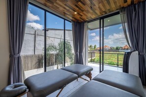 A room with two massage tables, large windows, and a view of a residential area. - Chic 4BR Villa w/ Private Massage Room & Huge Pool (Badung Regency)