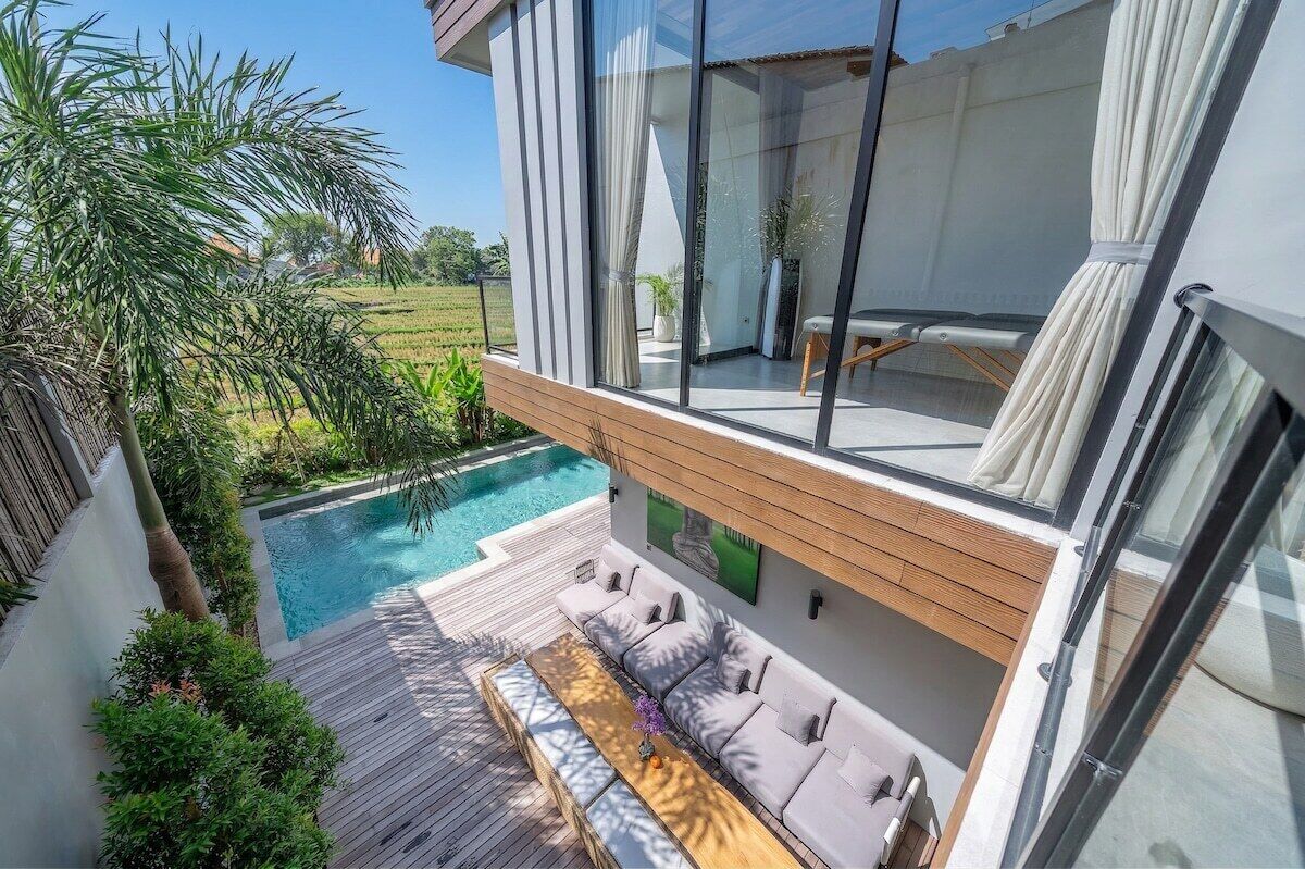 Une maison moderne dotée d’un balcon en verre donnant sur une piscine et une végétation luxuriante.