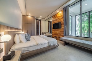 A modern bedroom with a large bed, bedside tables, a TV mounted on the wall, and a window with a view of greenery. - Chic 4BR Villa w/ Private Massage Room & Huge Pool (Badung Regency)