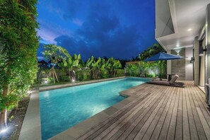 A swimming pool with a wooden deck and lounge chairs, surrounded by lush greenery. - Chic 4BR Villa w/ Private Massage Room & Huge Pool (Badung Regency)