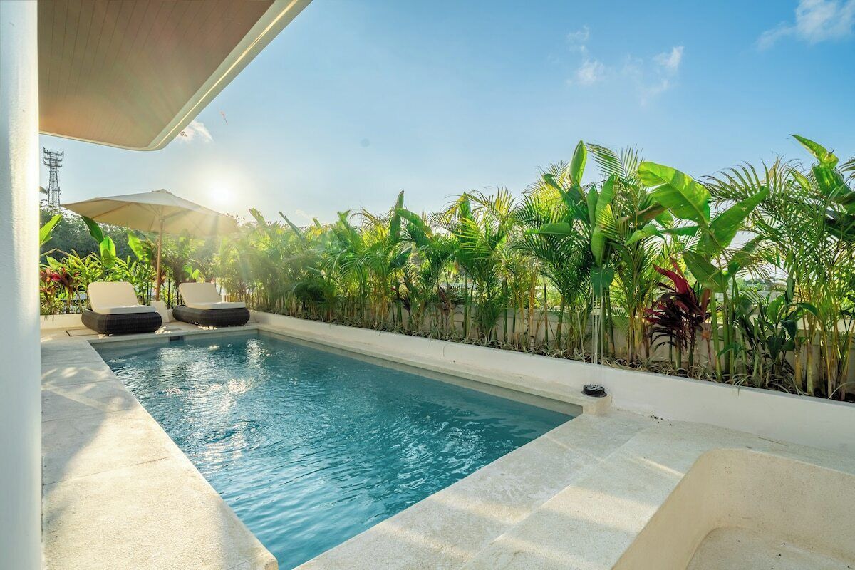 Una piscina con sillas de descanso, rodeada de plantas tropicales.