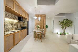 A modern kitchen with a stone backsplash, wooden cabinets, and a dining area with a table and chairs. - New Tropical 3BR Villa+Private Pool+Best Location (South Kuta)