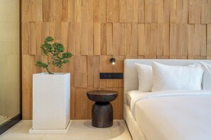 Ein Schlafzimmer mit einer Wandpaneele aus Holz, einem weißen Nachttisch mit einem Blumentopf, einem runden schwarzen Beistelltisch und einem Bett mit weißer Bettwäsche.