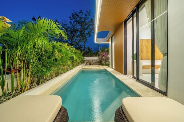 A modern pool area with a clear view of the pool, surrounded by lush greenery and a contemporary building with large windows. - New Tropical 3BR Villa+Private Pool+Best Location (South Kuta)