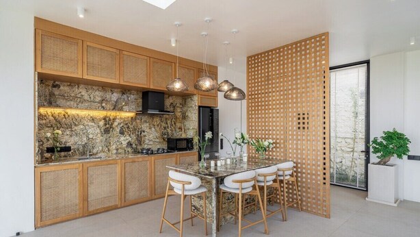 A modern kitchen with a stone backsplash, wooden cabinets, and a central island with bar stools. - New Tropical 3BR Villa+Private Pool+Best Location (South Kuta)