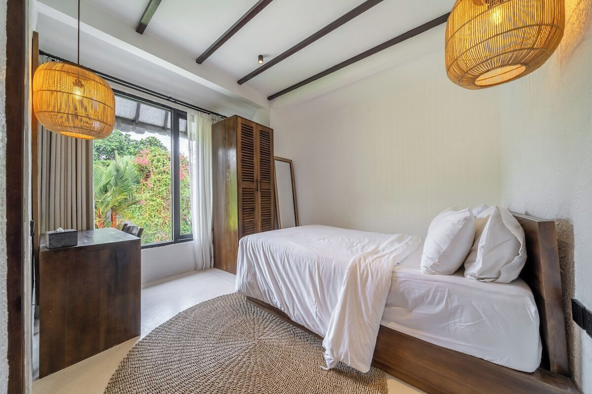 A bedroom with a bed, a desk, and a window with curtains.