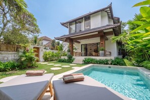 Ein modernes Haus mit Schwimmbad, Liegestühlen und einem gepflegten Garten.