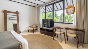 A modern bedroom with a bed, a TV, a wooden chair, a sofa, and a large window with curtains. - Designer 3BR Stay in Ubud • Pool • Patio • Garden (Gianyar Regency)