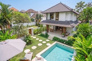 Ein Haus mit Swimmingpool, einer Terrasse mit Gartenmöbeln und einem Garten mit verschiedenen Pflanzen.