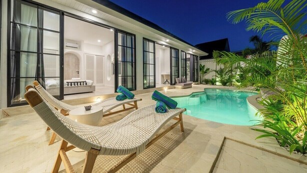 Ett modernt hus med en swimmingpool, solstolar och en väl upplyst interiör.