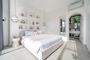 Ein modernes Schlafzimmer mit einem großen Bett, Nachttischen, einer integrierten Ablage mit Dekoration und Blick durch einen Bogen.