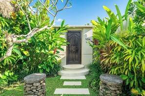 Eine Villa mit Eingang, einer dunklen Holztür, einem Steinweg und üppiger tropischer Bepflanzung.
