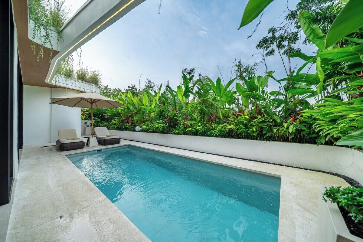 Ein Swimmingpool mit Liegestühlen und Sonnenschirm, umgeben von üppigem Grün.