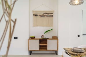 Une pièce au décor minimaliste, avec un meuble en bois, une décoration murale en macramé et une plante en pot.