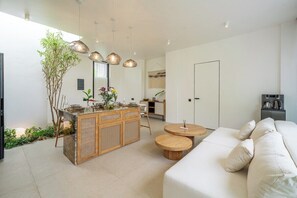 A modern living room with a sofa, a wooden dining table, and a kitchen area in the background. - Chic 2BR Villa in a Prime Location w Pool & Garden (Badung Regency)
