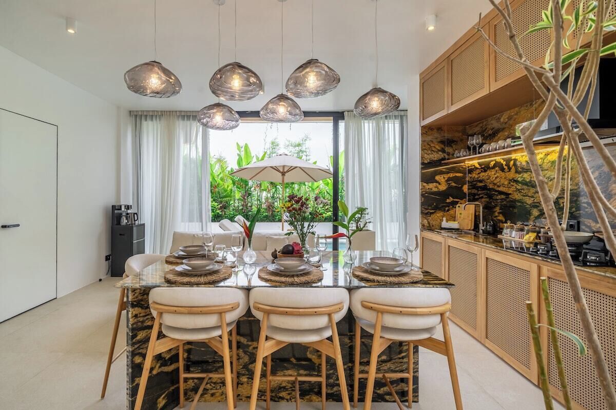 Un espace repas moderne avec une table en verre, des chaises blanches et une vue sur la verdure environnante.