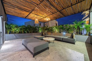 Un área de estar al aire libre con un diseño moderno, que incluye una sección cubierta con techo de madera e iluminación ambiental.