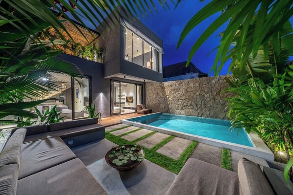 Una casa moderna con piscina, paredes de piedra y mobiliario de exterior.