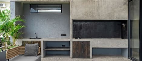 Un área de cocina exterior moderna con una parrilla empotrada, asientos y un ventanal grande.