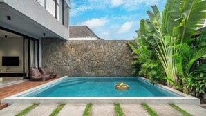 Een modern huis met een zwembad, een stenen muur en weelderige tropische planten.