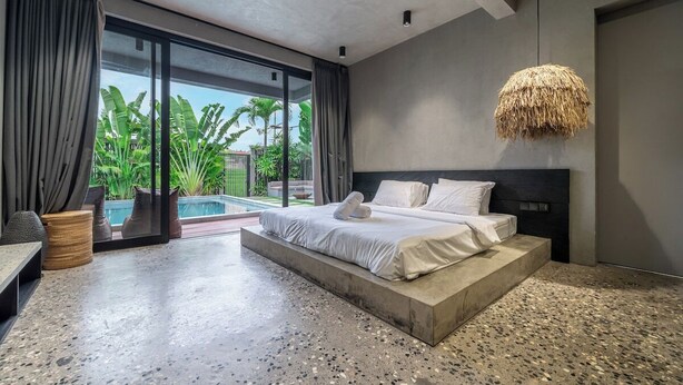 Een moderne slaapkamer met een groot bed, uitzicht op een zwembad en een betonnen vloer.