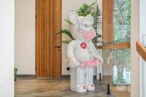 A white bear statue with a pink bow tie standing in a hallway with a wooden door and a plant in the background. - Jungle 9BR Ubud Paradise with spa! (Ubud)
